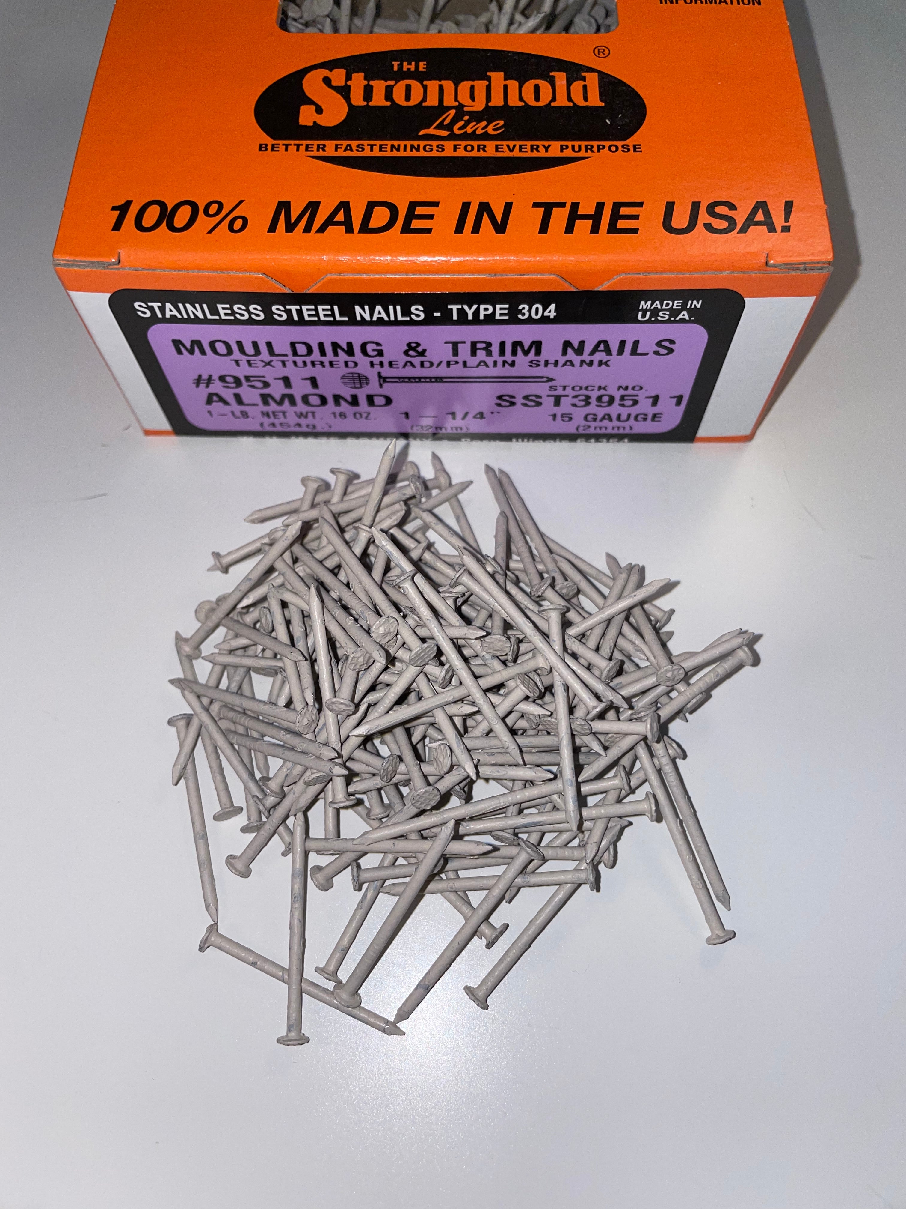 A box of Stainless Steel Trim Nails with a pile of loose nails in front of it. The nails are Almond in color.