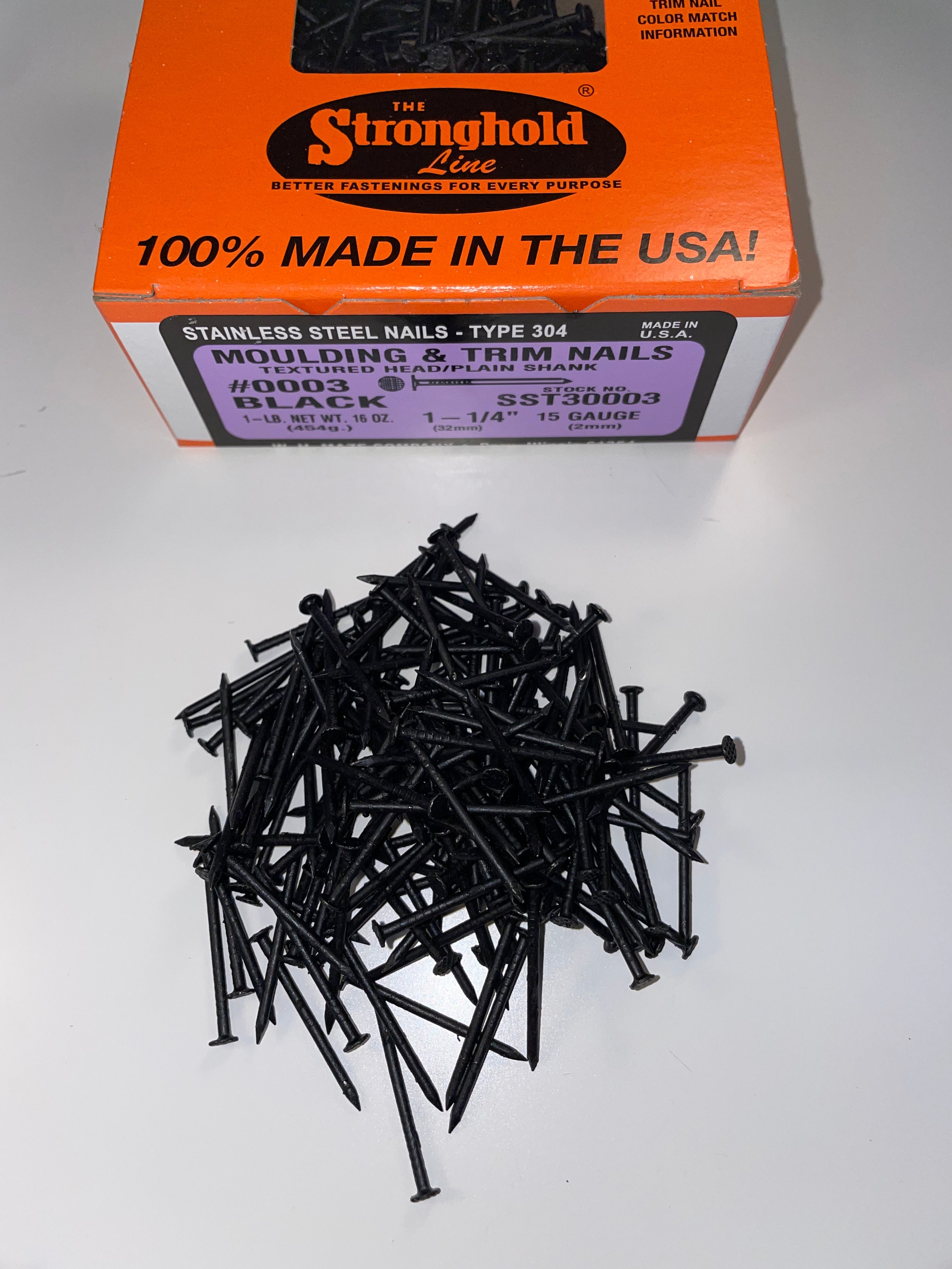 A box of Stainless Steel Trim Nails with a pile of loose nails in front of it. The nails are Black in color.