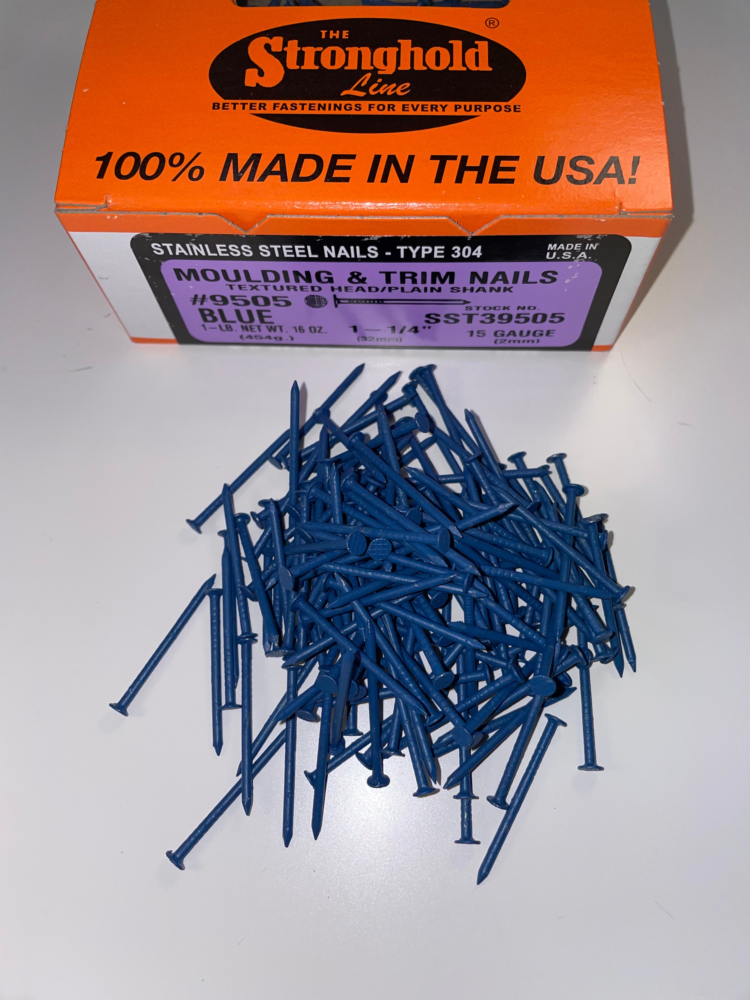 A box of Stainless Steel Trim Nails with a pile of loose nails in front of it. The nails are Midnight Blue in color.