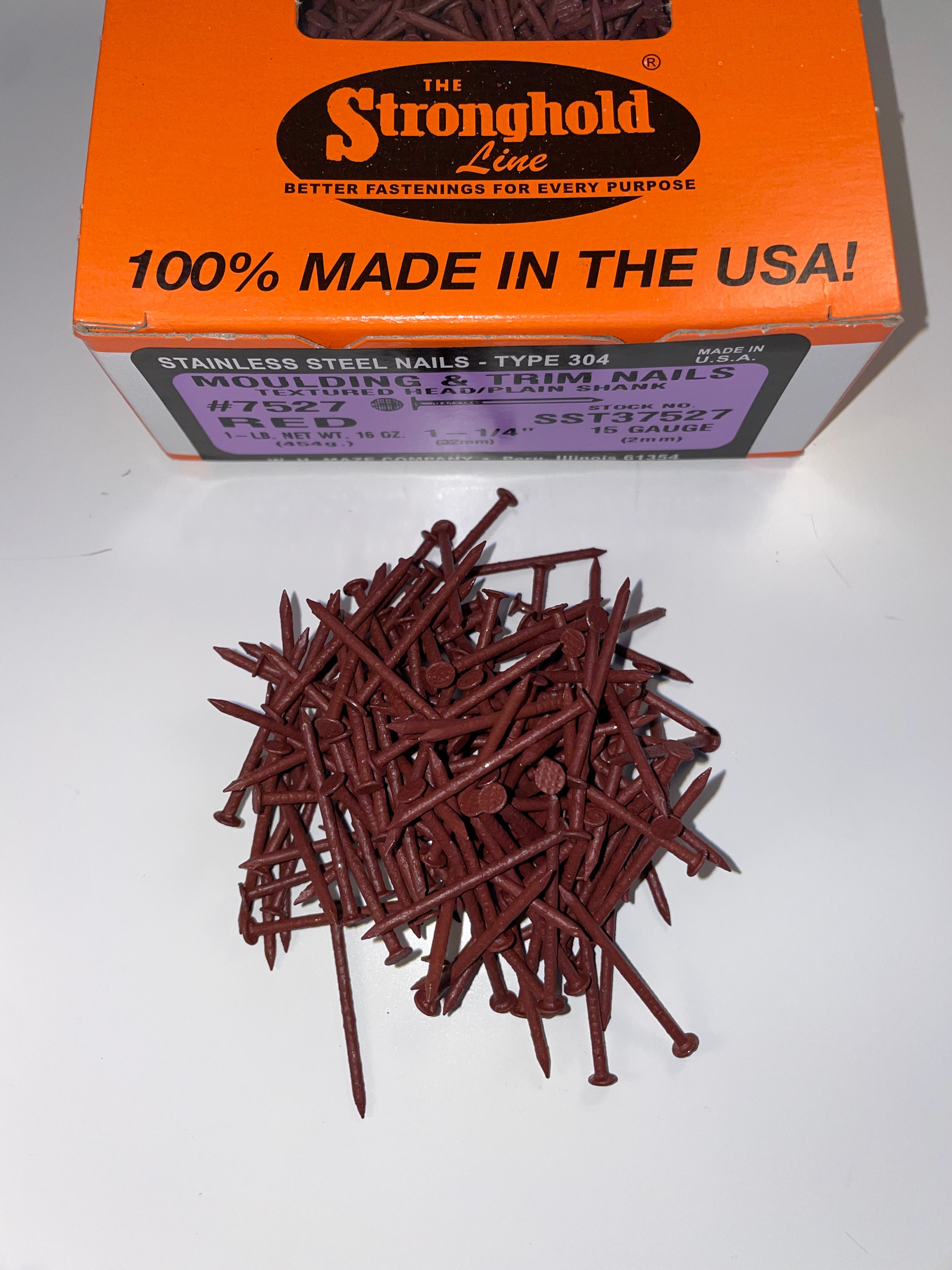 A box of Stainless Steel Trim Nails with a pile of loose nails in front of it. The nails are Burgundy in color.