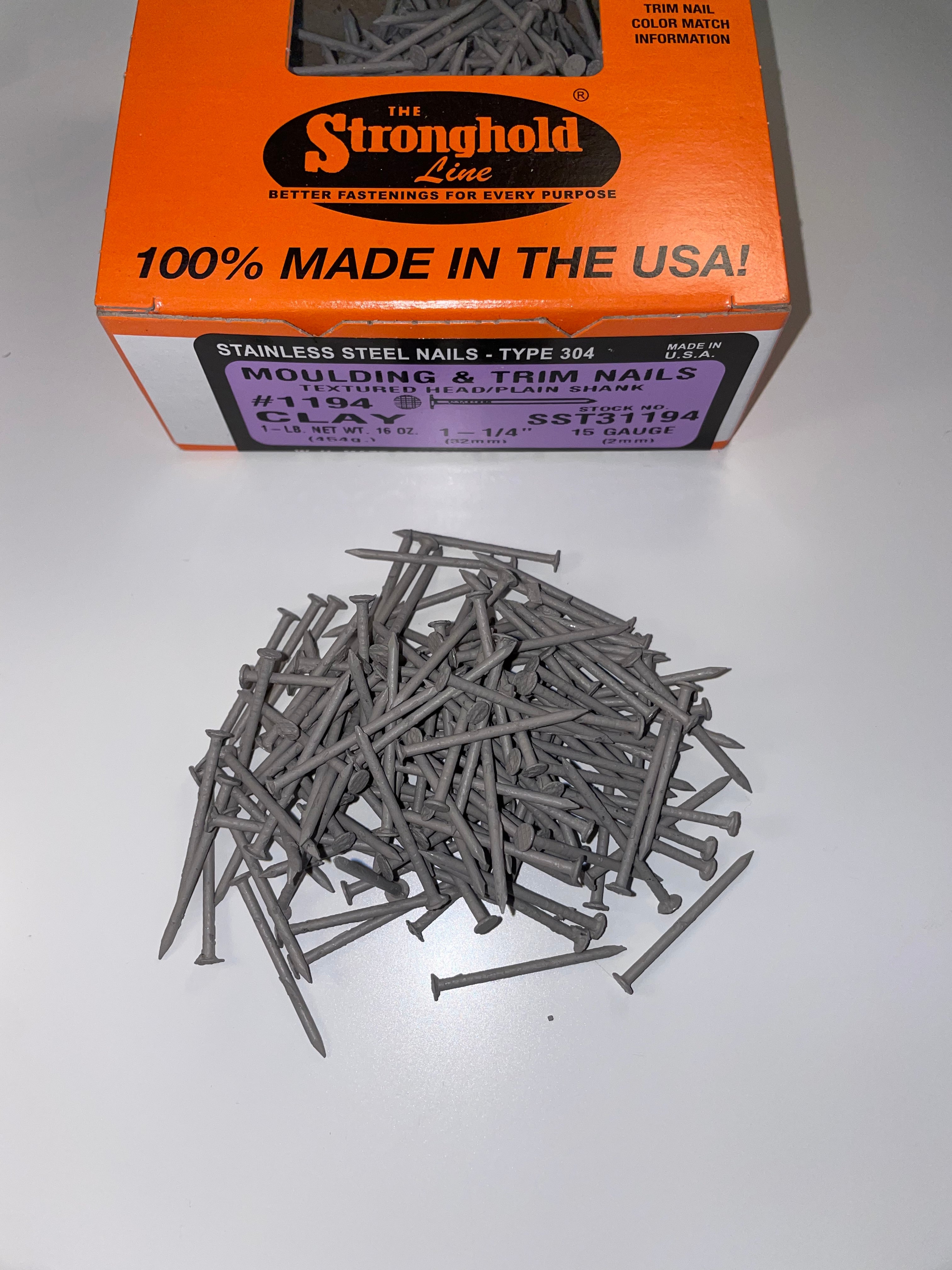 A box of Stainless Steel Trim Nails with a pile of loose nails in front of it. The nails are Clay in color.