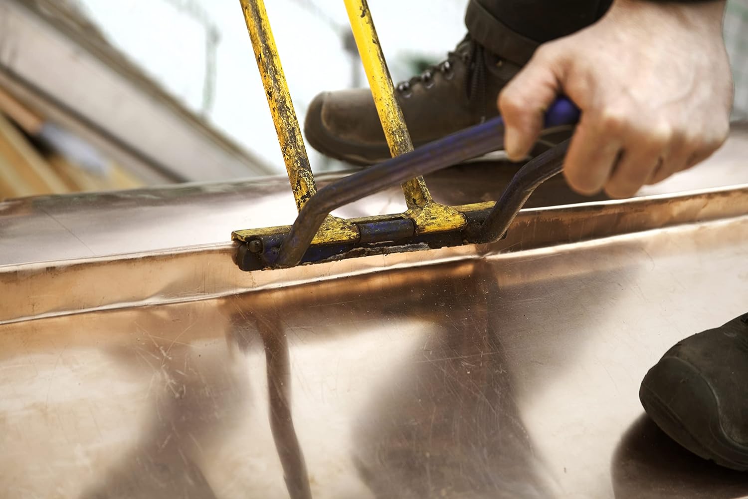 Copper flashing being bent and seamed with a sheet metal hand tool.