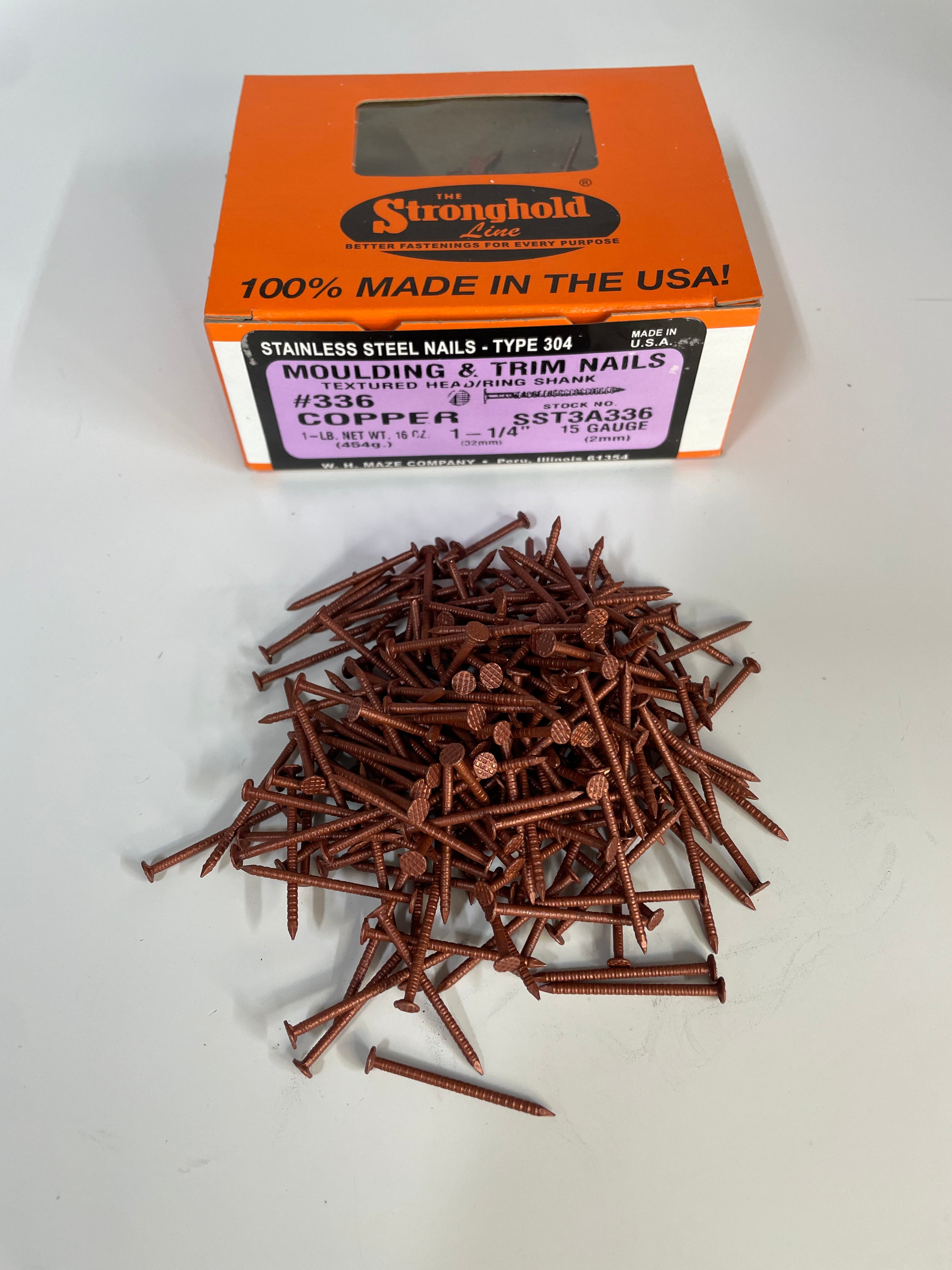A box of Stainless Steel Trim Nails with a pile of loose nails in front of it. The nails are Copper Metallic in color.