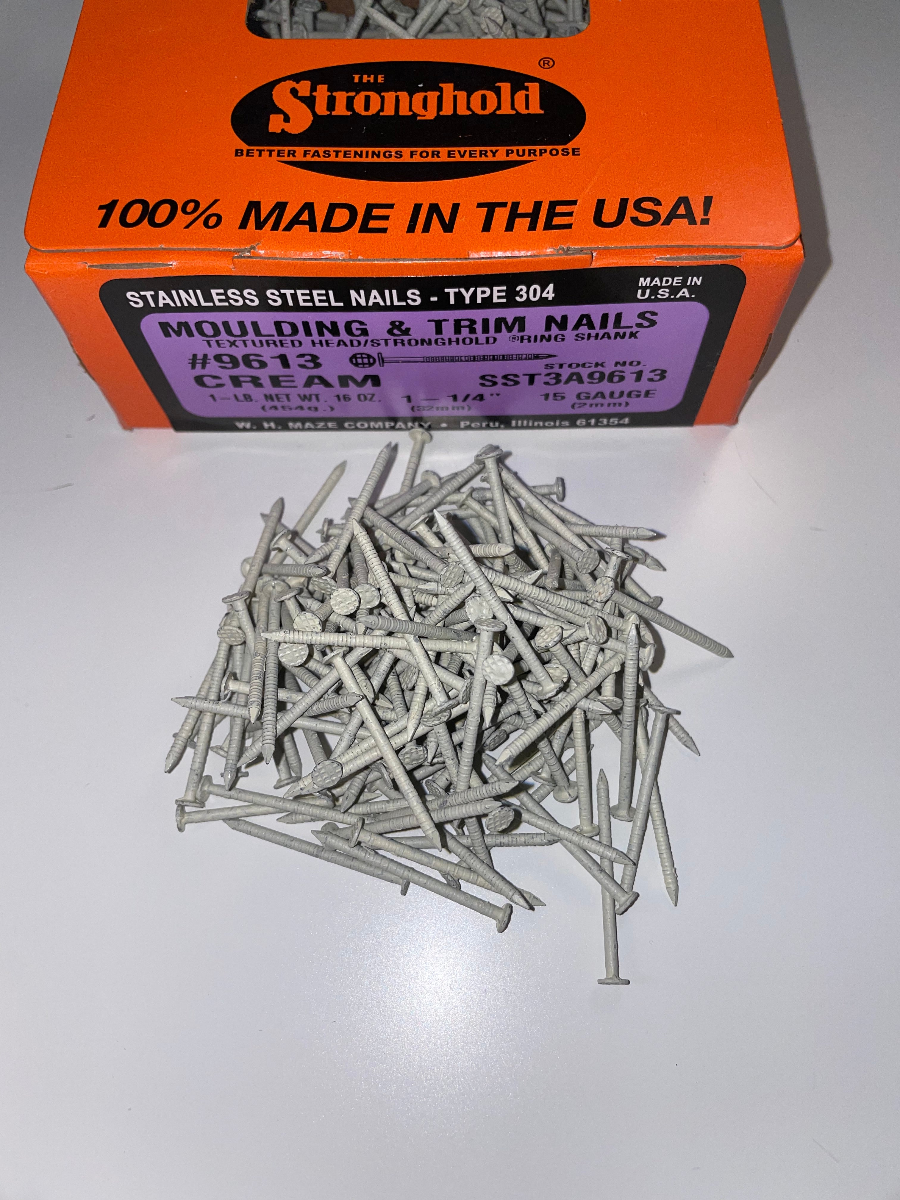 A box of Stainless Steel Trim Nails with a pile of loose nails in front of it. The nails are Cream in color.