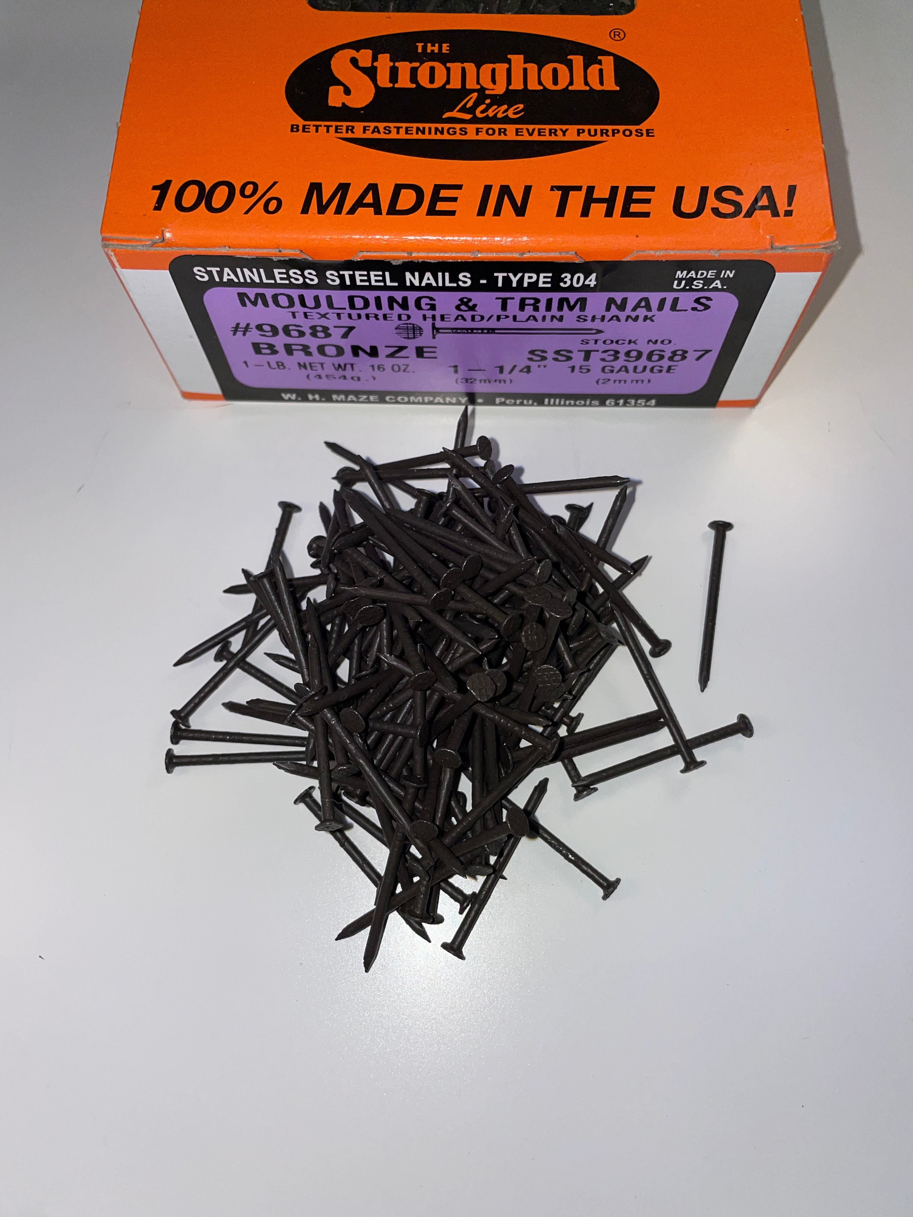 A box of Stainless Steel Trim Nails with a pile of loose nails in front of it. The nails are Dark Bronze in color.