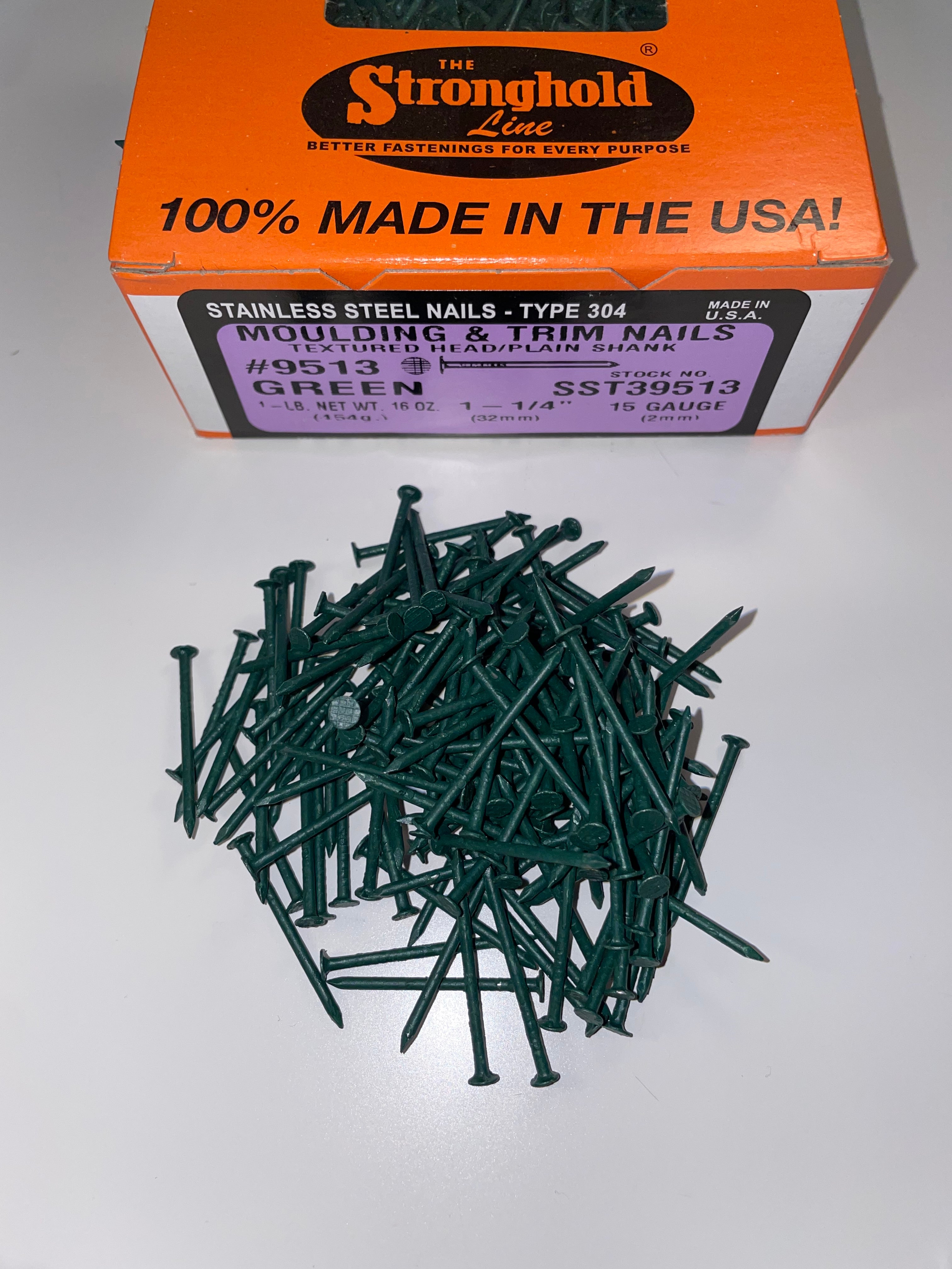 A box of Stainless Steel Trim Nails with a pile of loose nails in front of it. The nails are Grecian Green in color.