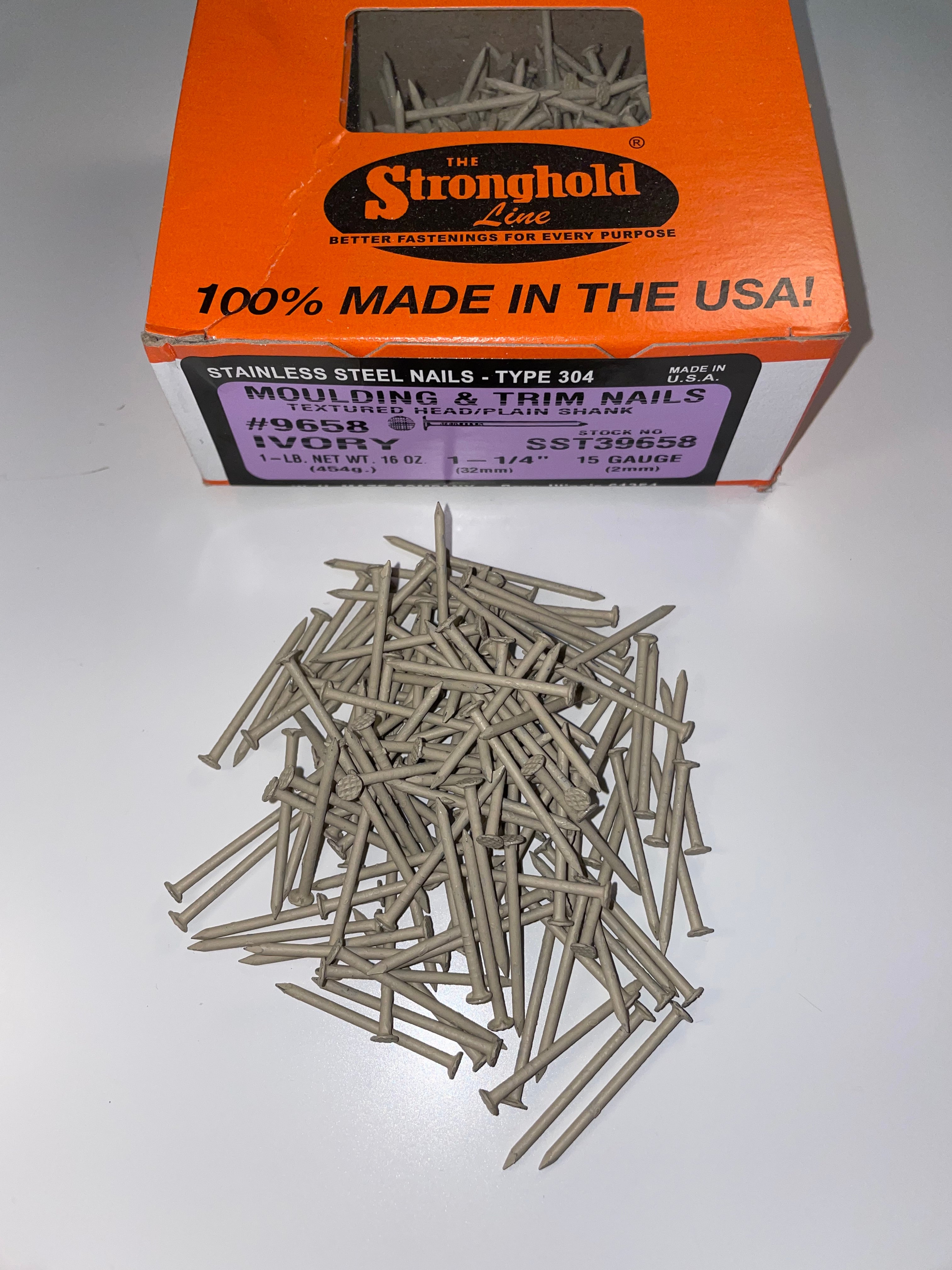 A box of Stainless Steel Trim Nails with a pile of loose nails in front of it. The nails are Ivory in color.