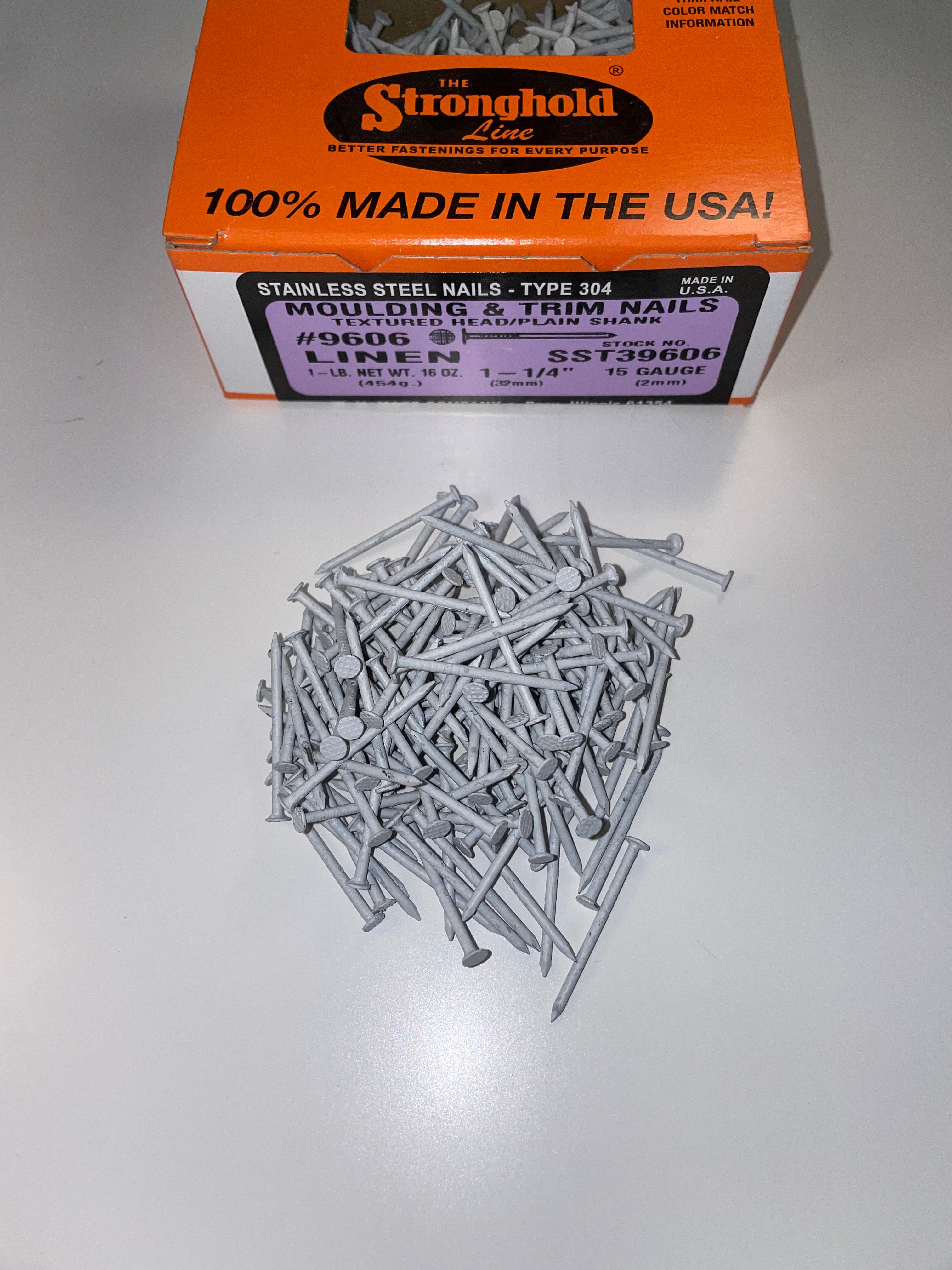 A box of Stainless Steel Trim Nails with a pile of loose nails in front of it. The nails are Linen in color.