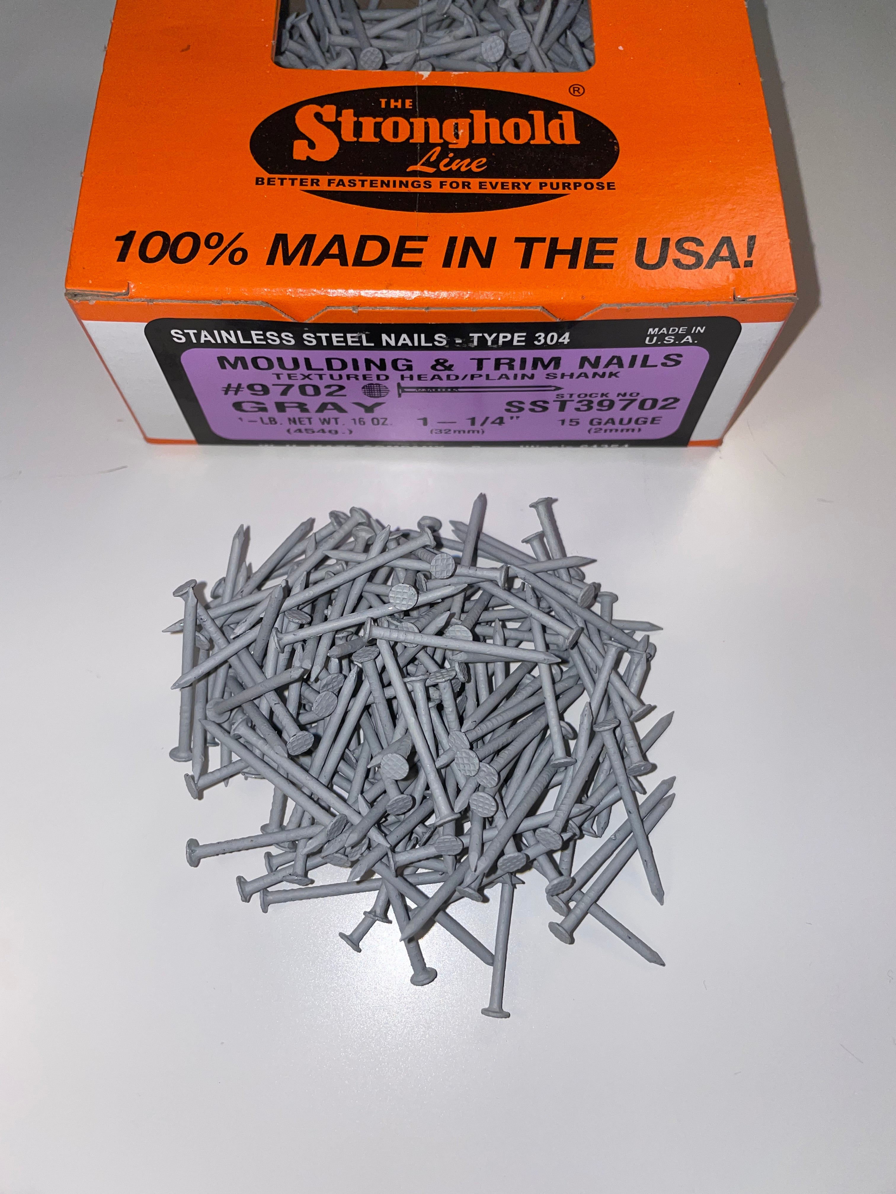 A box of Stainless Steel Trim Nails with a pile of loose nails in front of it. The nails are Pearl Gray in color.