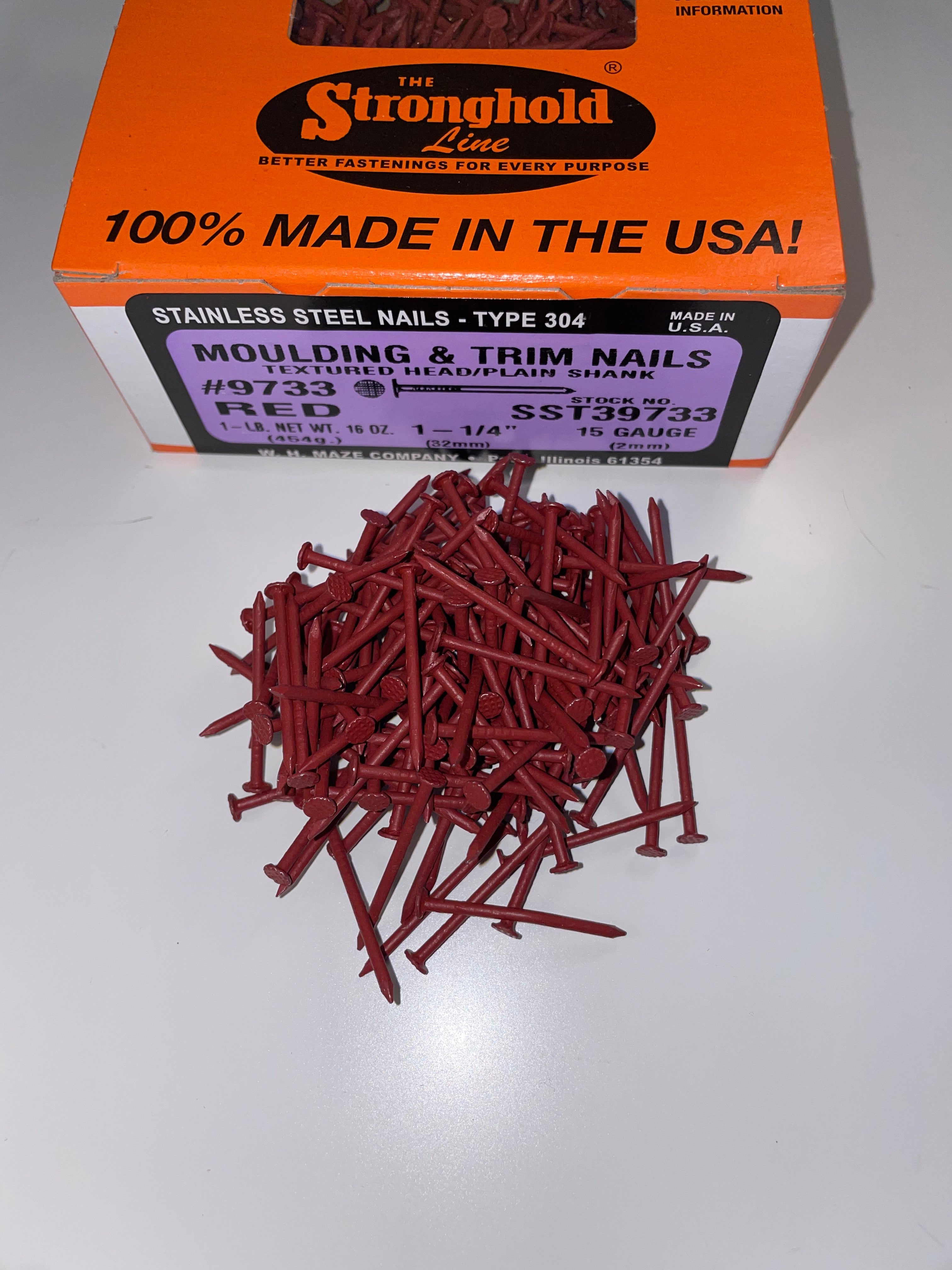 A box of Stainless Steel Trim Nails with a pile of loose nails in front of it. The nails are Bright Red in color.