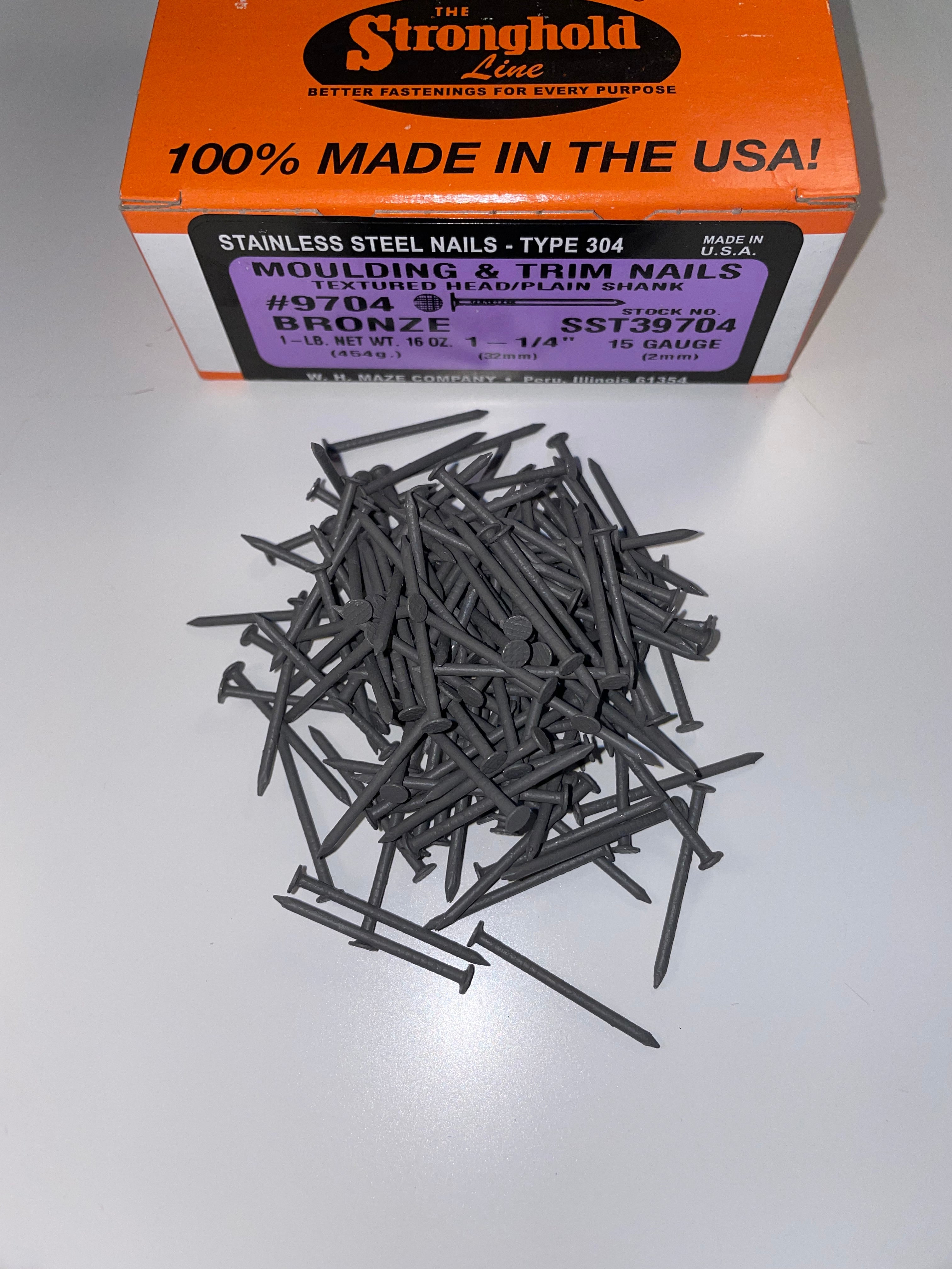 A box of Stainless Steel Trim Nails with a pile of loose nails in front of it. The nails are Terratone in color.