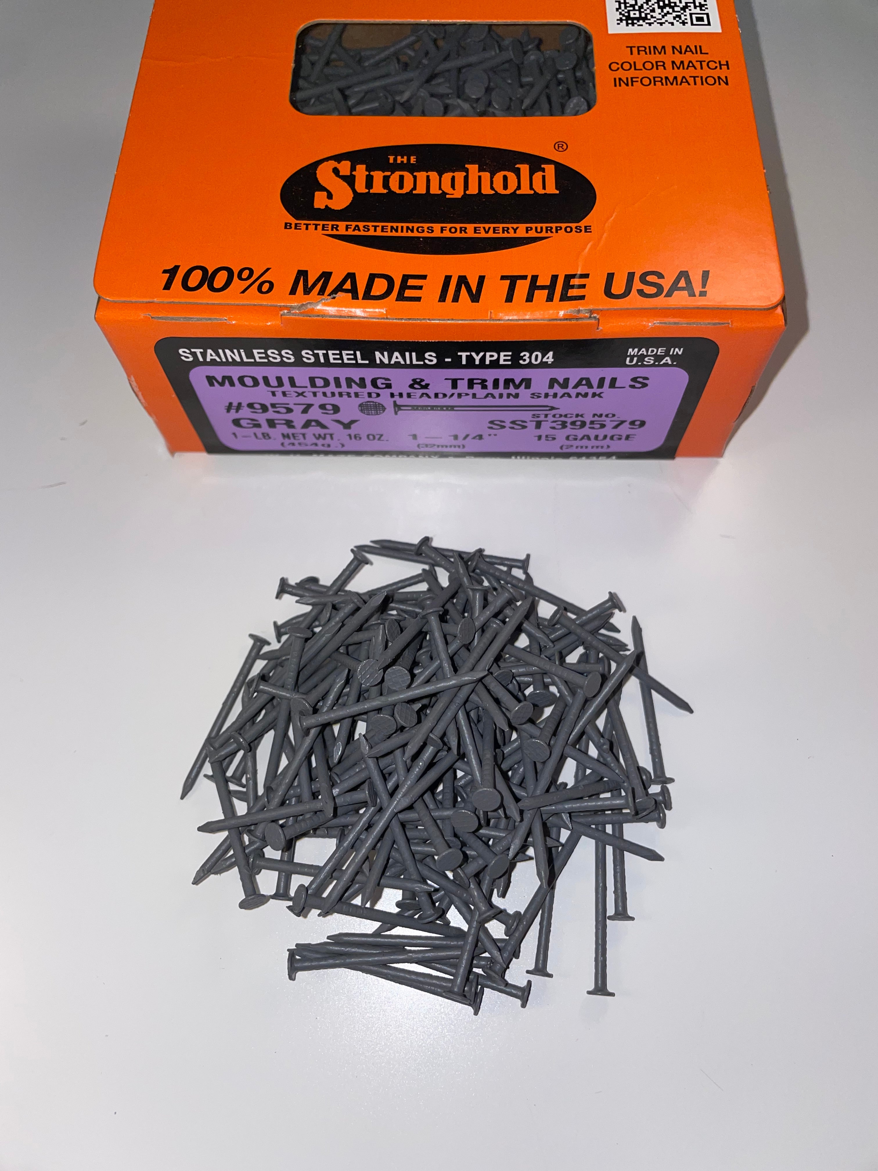 A box of Stainless Steel Trim Nails with a pile of loose nails in front of it. The nails are Tuxedo Gray in color.