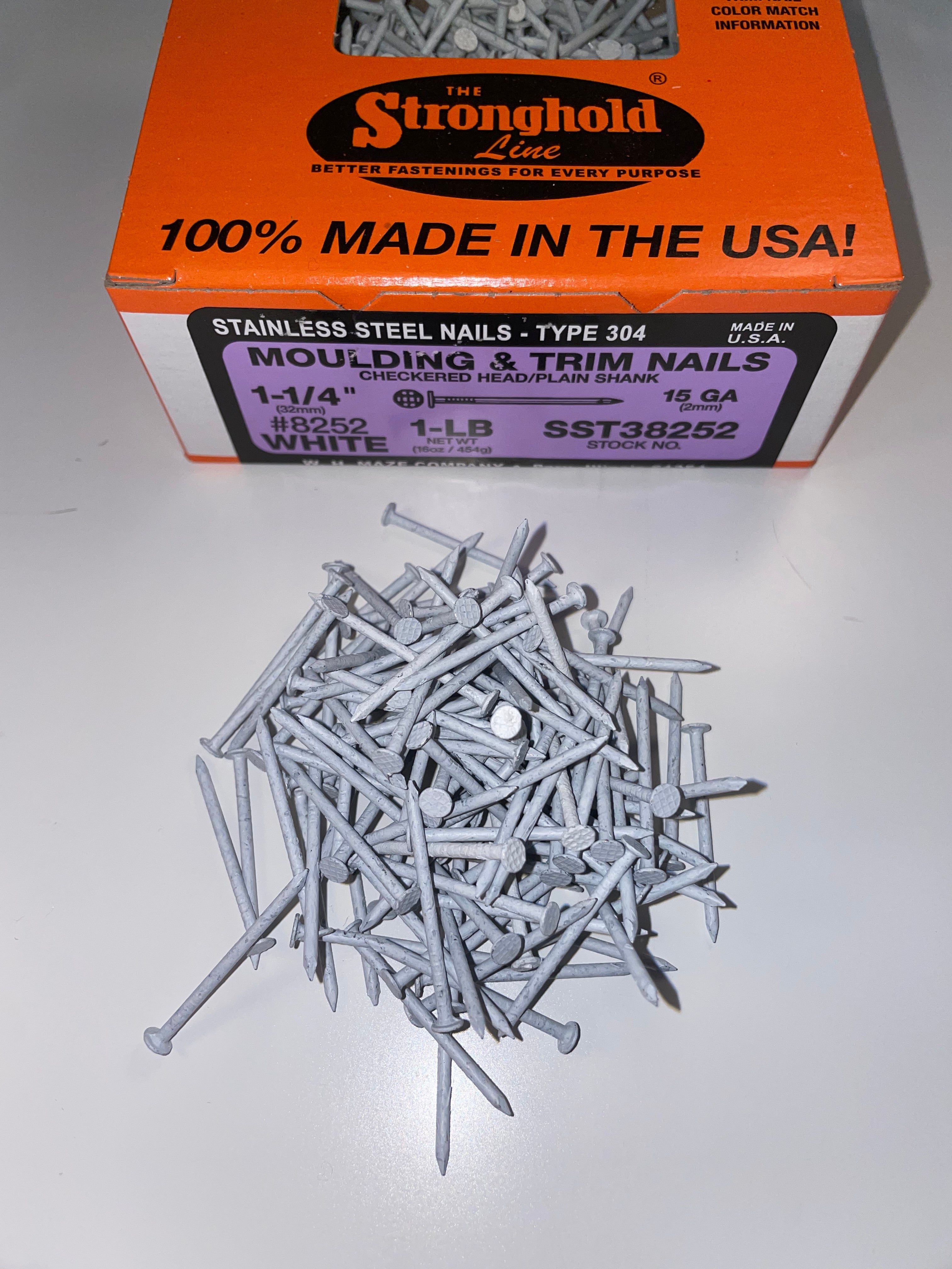 A box of Stainless Steel Trim Nails with a pile of loose nails in front of it. The nails are White in color.